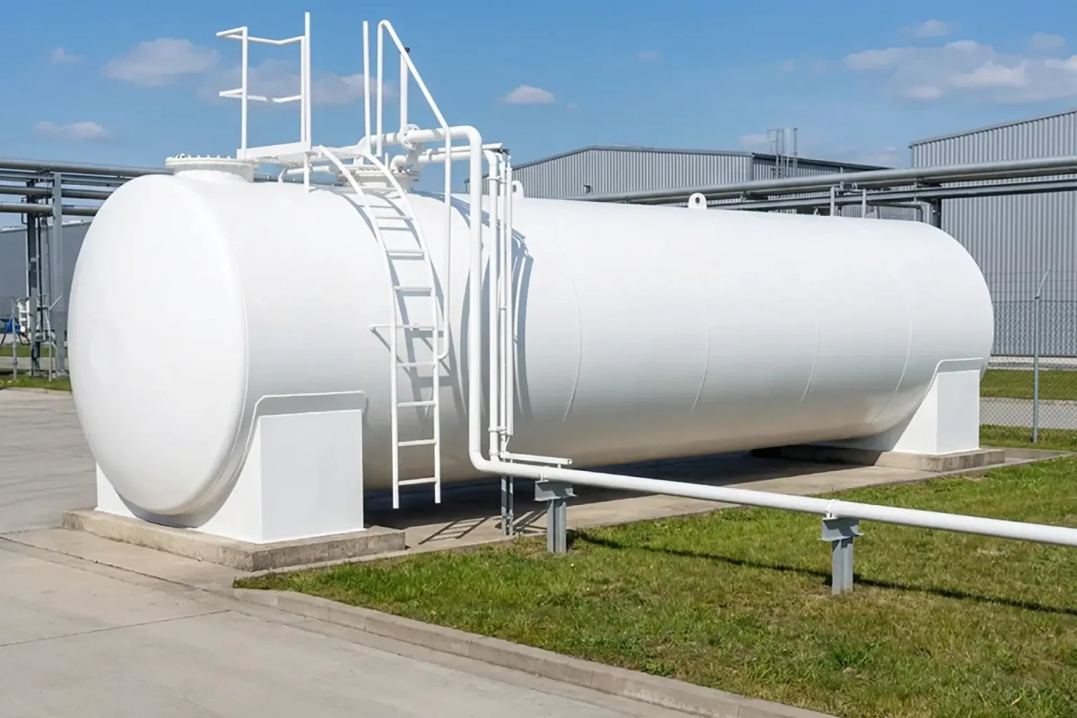Stor vit horisontell industriell lagringstank med stege och rörledningar