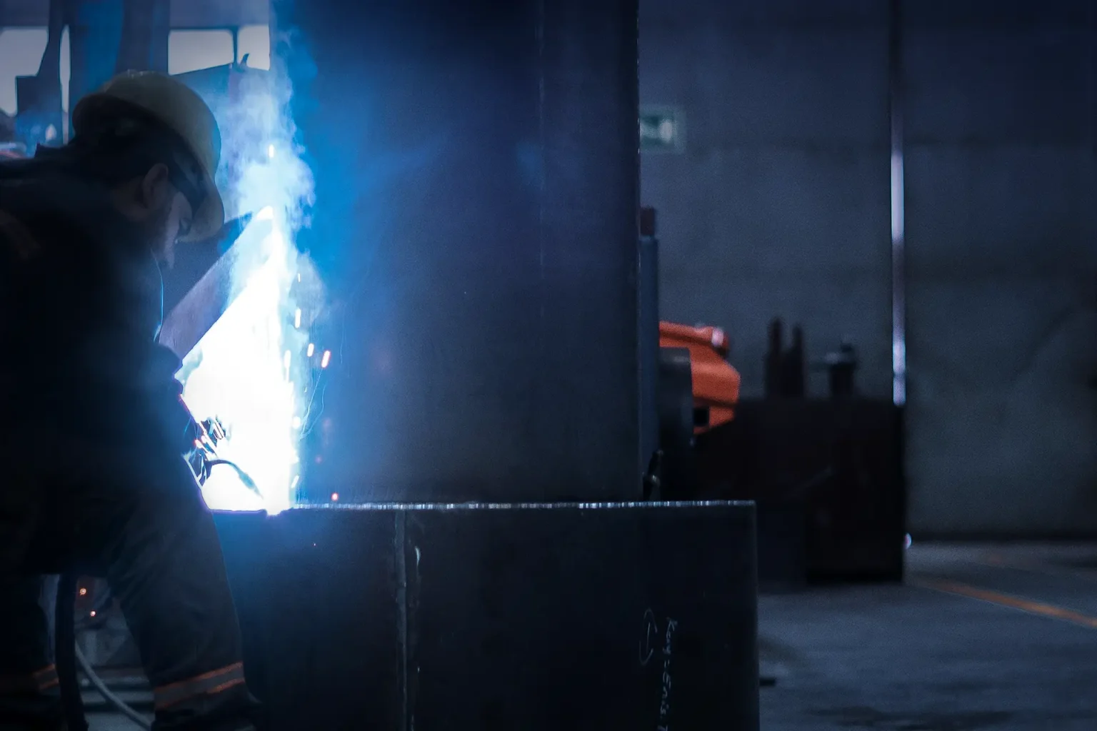 En arbetare i skyddshjälm svetsar en stor metallkonstruktion i en fabrik